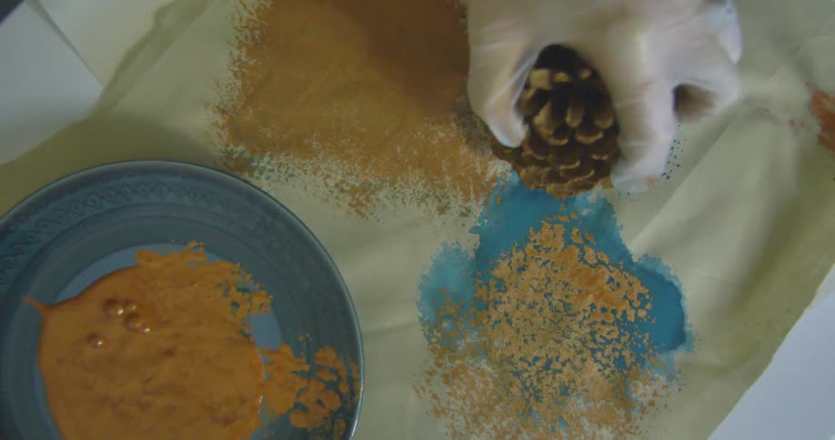 A person is making art with paint and a pinecone
