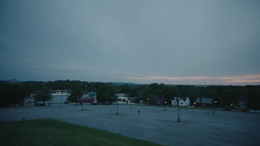 Teenager riding a skateboard on an empty parking lot on a small town at sunset