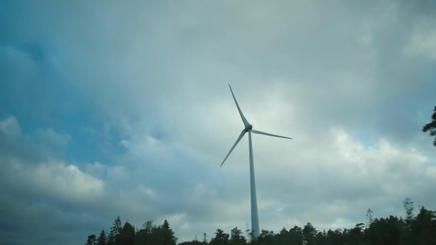 Silhouette of a wind turbine slowly turning against a blue sky at evening