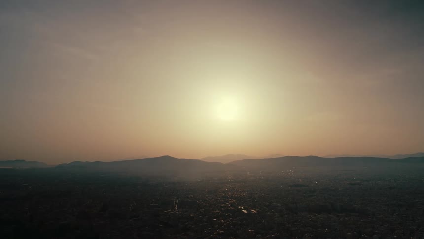 The sun is shining brightly above mountains in a hazy orange sky