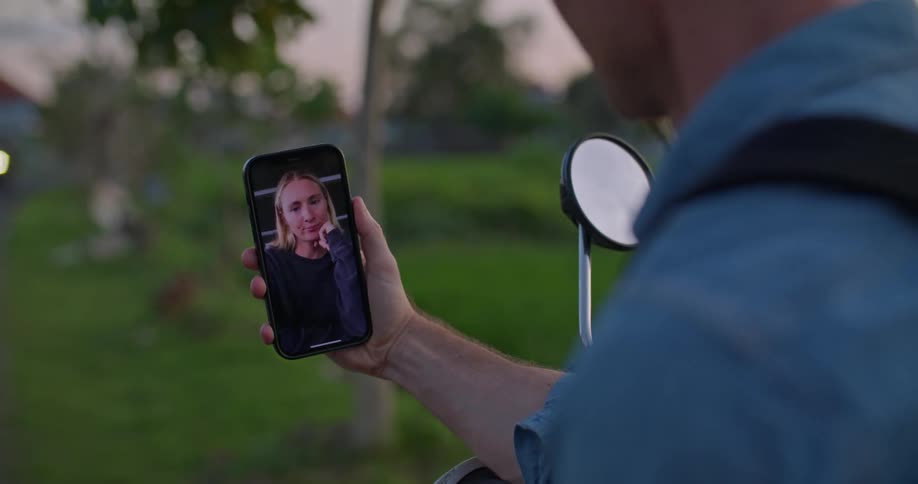 Man talking to a woman on a smartphone video call on a rural field at evening