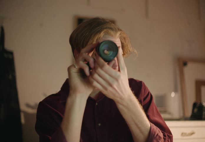 Male photographer with beard and red shirt checks his camera lenses
