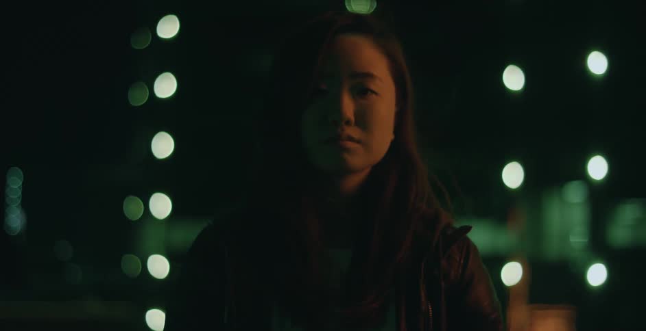 Woman with dark hair and black jacket looks at camera at night