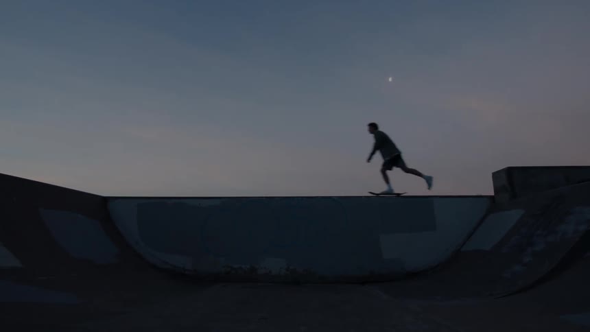 Silhouette of a teenager riding a skateboard on an empty skate park on a small town at evening