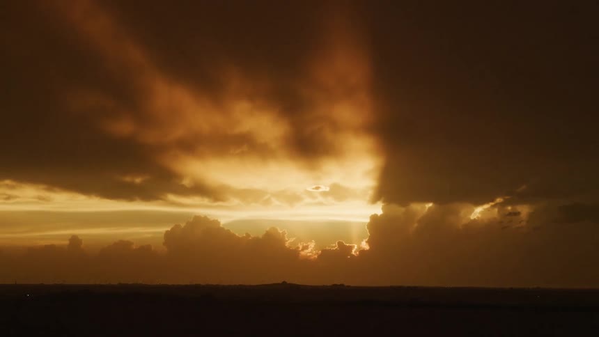 Time lapse of sun setting and god rays emerging with towering cumulous clouds in this golden light shot