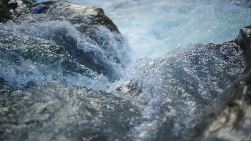River water flowing over rocks splashing and foaming on a bright sunny day