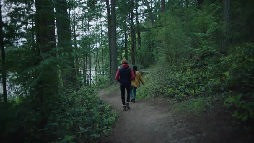 Man and woman walk on a dirt path in the forest next to a lake