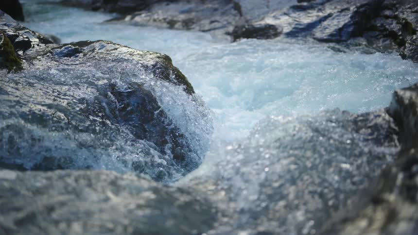Turbulent water on a river rapids flowing over big rocks at daytime