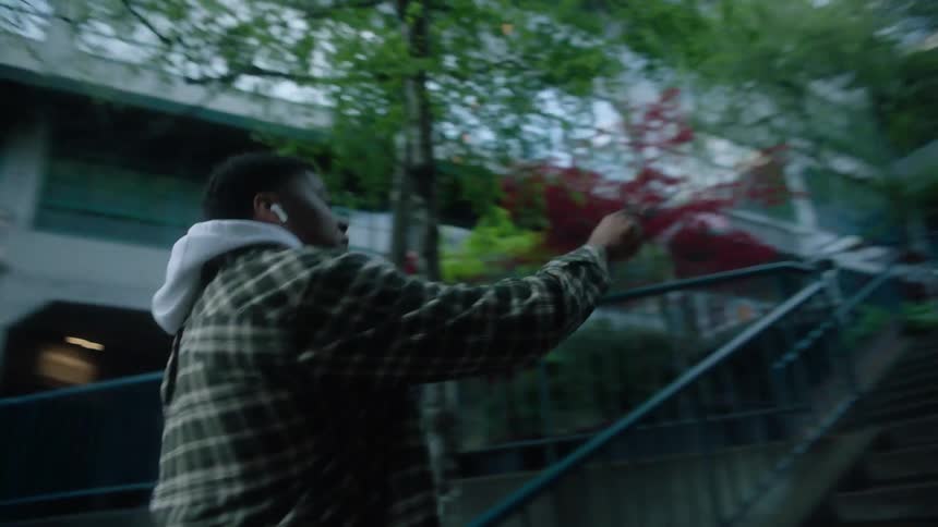 Man with white hoodie green jacket and earphones dances and goes up the stairs in the public park