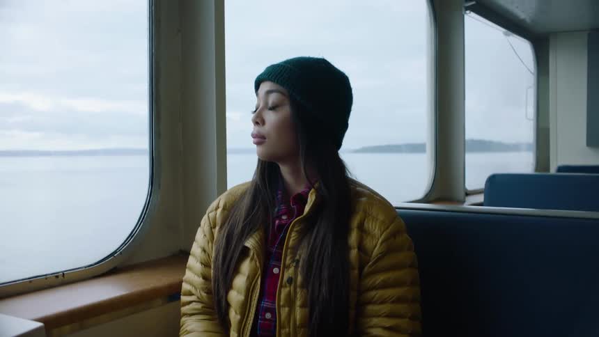 A woman sitting on a bench seat on a ferry looking out the window