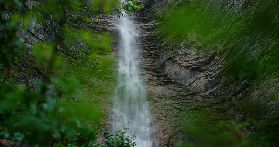 Waterfalls are flowing down the side of a mountain cliff and there are trees and woods below