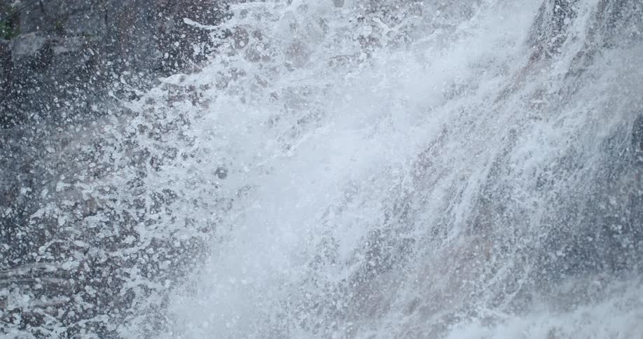 Tall waterfall flowing down the rugged barren rock surface of a cliff on the mountains