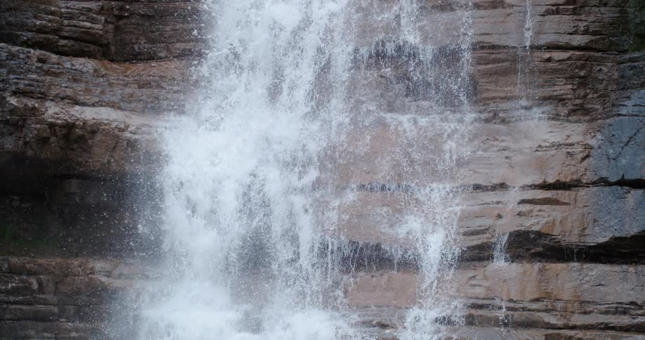 Waterfall flows down tall cliff wall with several crevices