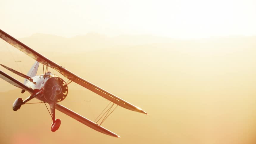 A biplane flying at sunset coming in and out of frame in beautiful evening sunlight