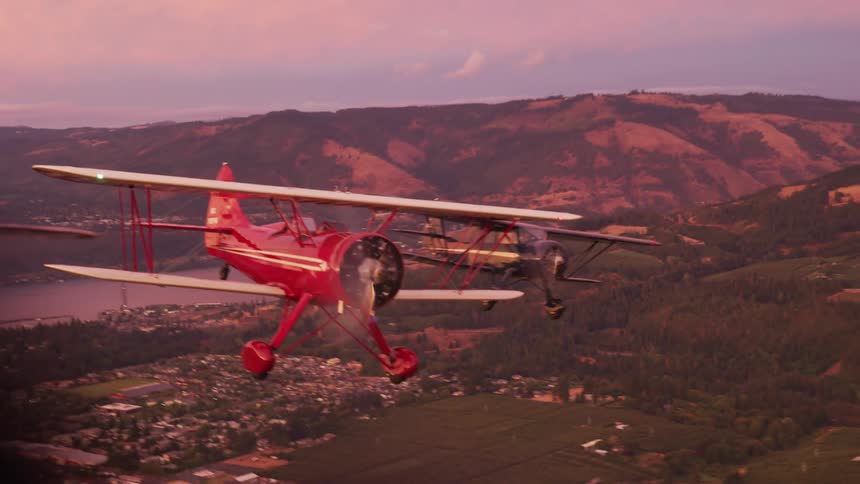 Passenger perspective as three vintage biplanes fly over a beautiful town at sunset in formation flight