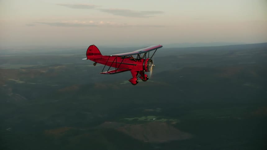 The Red biplane flying towards the setting sun and dives towards Mount Hood