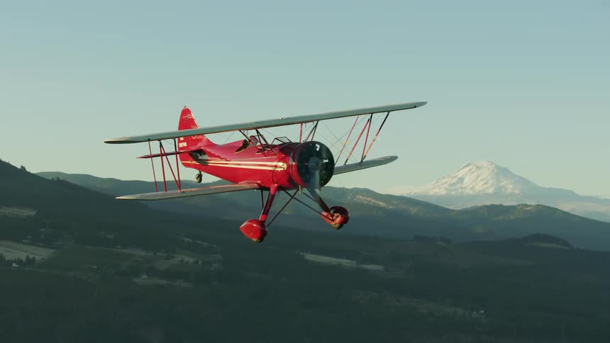 Propeller biplane flies over lake and the surrounding mountainous terrain on a clear summer day