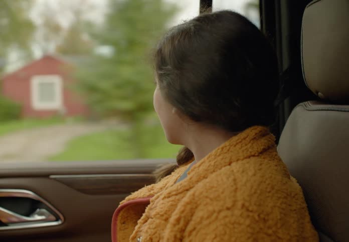 A woman is sitting in the passenger seat of an automobile looking out the window as they pass houses and trees