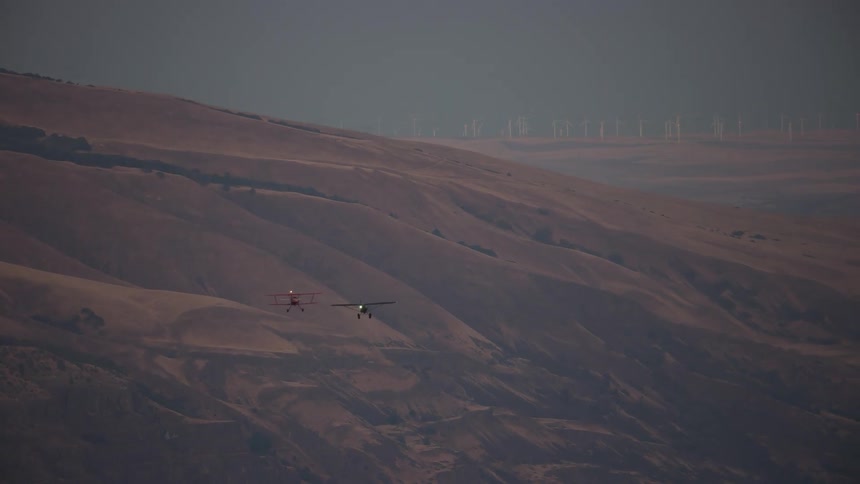 Two old planes flying low in front of a mountain in the desert at evening