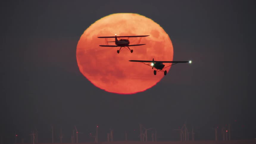A view of two planes flying in front of a moon