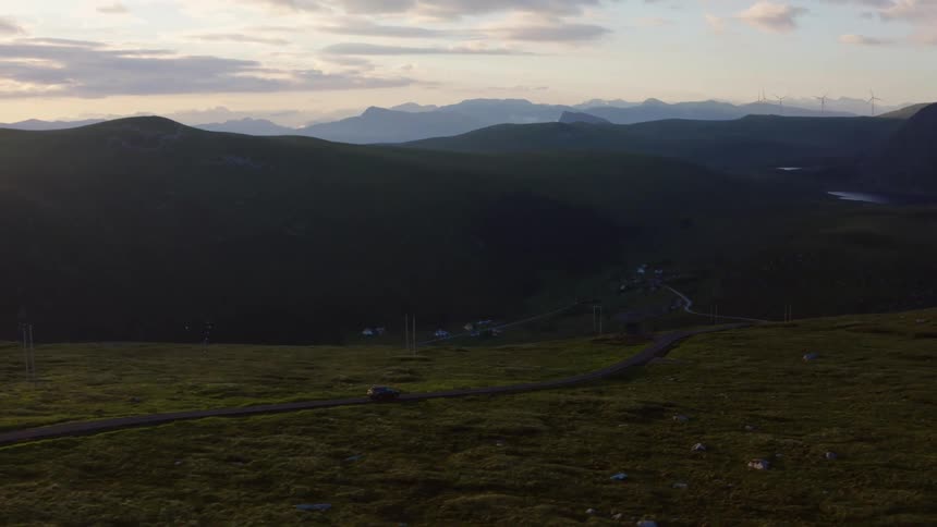 A vehicle drives down a country road past a neighborhood near a mountain range