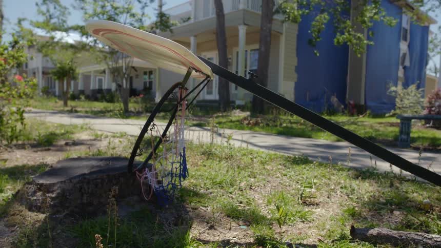 Fallen basketball hoop resting over a rock in the yard in front of a house