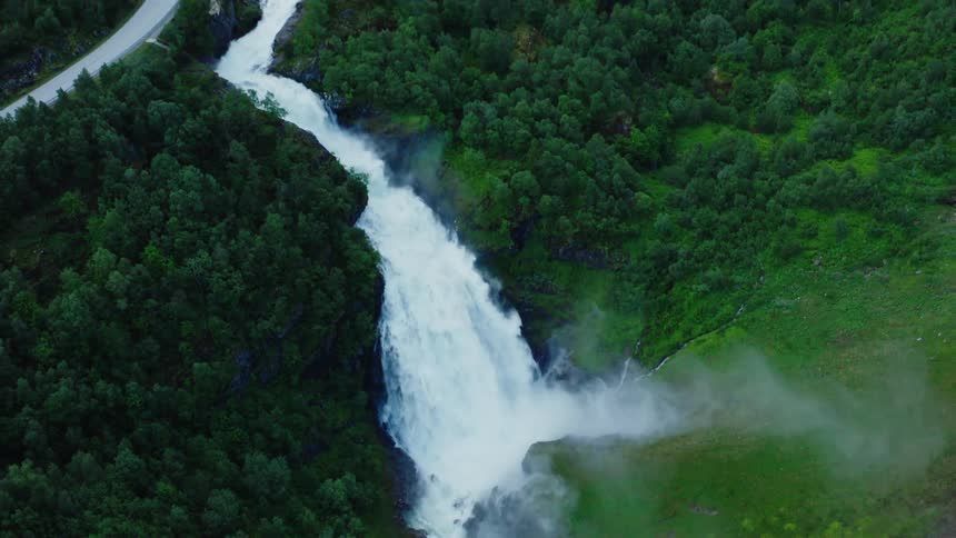 Waterfall flowing down of a cliff on the mountains surrounded by green lush vegetation close to a road