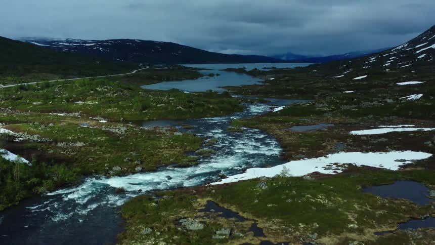 River forms rapids as it winds between snow dappled mountains under an overcast sky