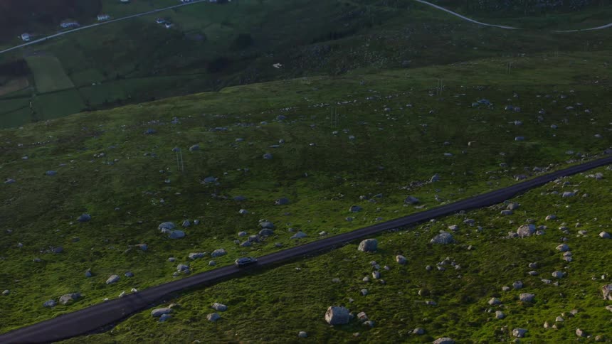 Car drives to a farm on a valley using a road in the mountains surrounded by large white boulders