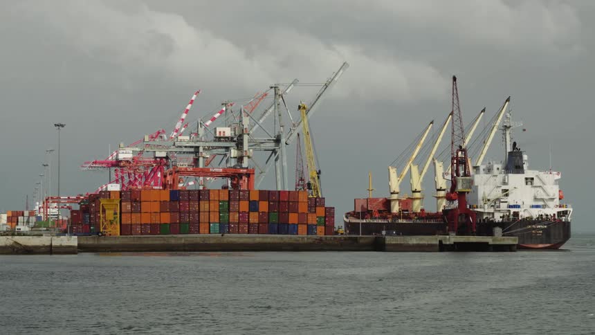 A cargo ship with cranes and many containers sits in the harbor