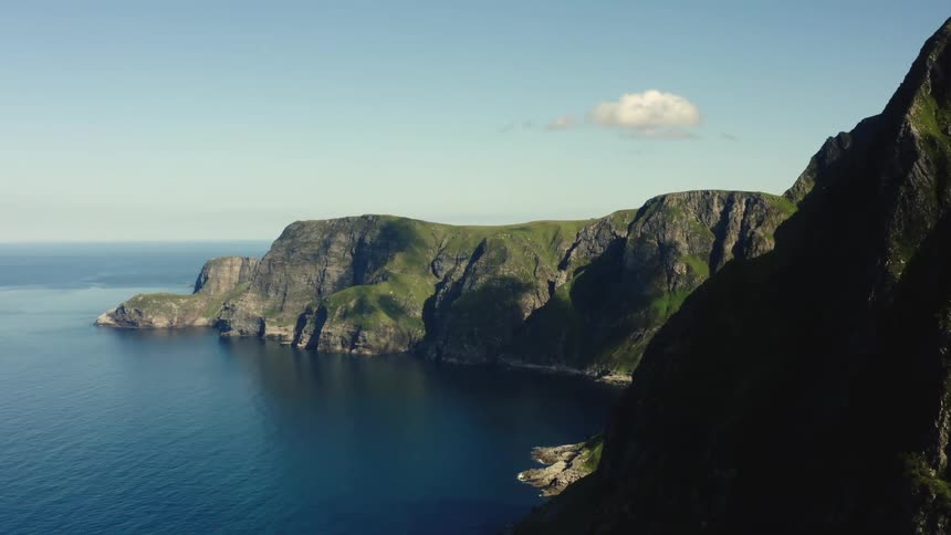 Aerial view of a promontory at the end of a mountain range next to the blue ocean water