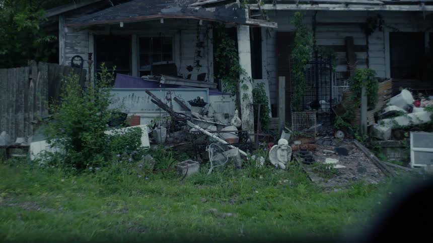 A damaged home with front yard full of junk and holes in the roof