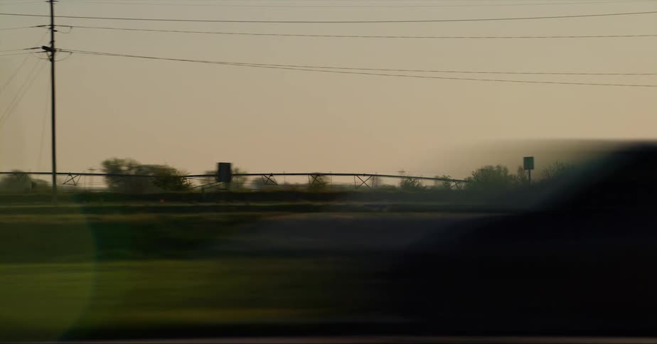 The sun is setting in a rural area that cars are driving by