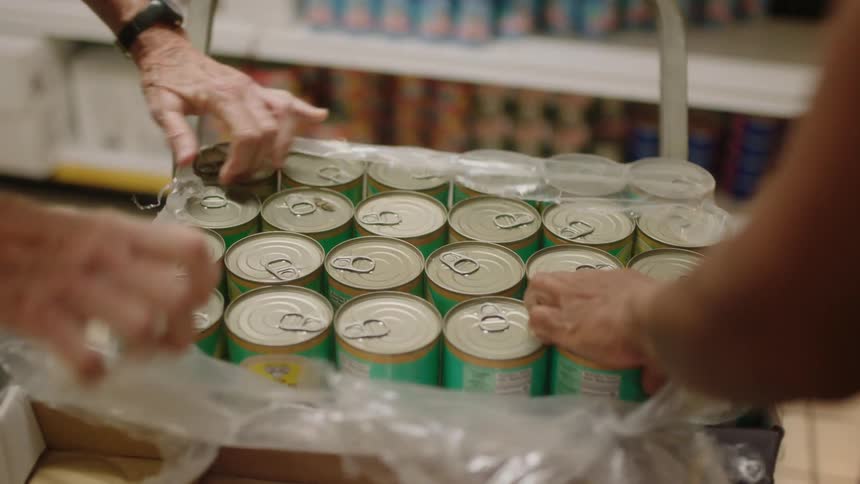 A man and a woman are working in a grocery store tearing the plastic off of a case of cans