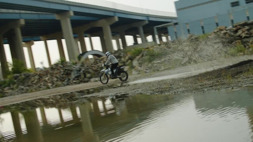 A man is riding a motorcycle under a bridge during spring