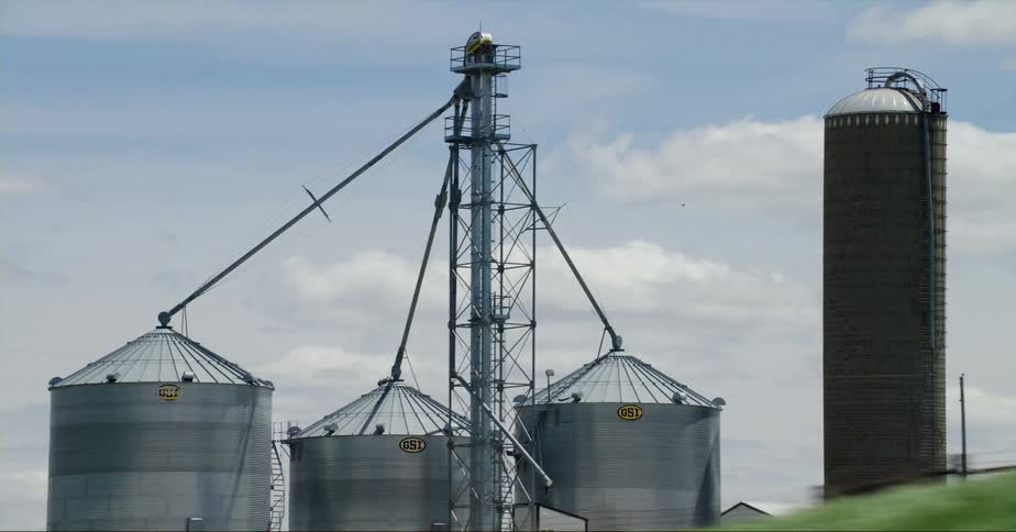 Three metallic grain silos are standing next to a tall brown storage tower on a farm