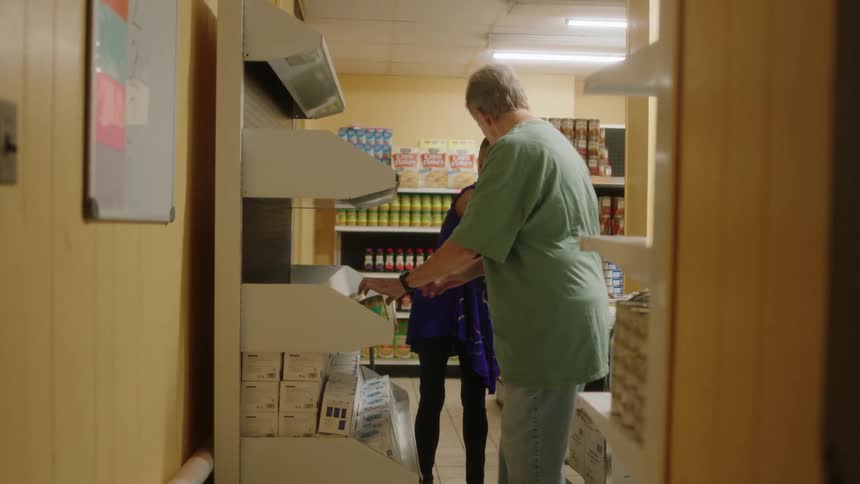 A man and a woman are working in a grocery store putting cans on a shelf