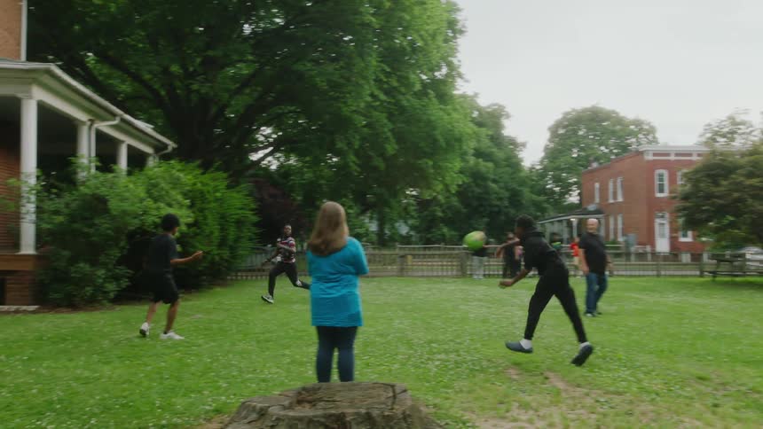 Family and friends playing a casual game of dodgeball over the green grass in the backyard at home