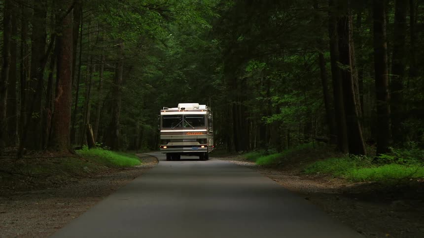 A recreational vehicle travels down a road surrounded by woods
