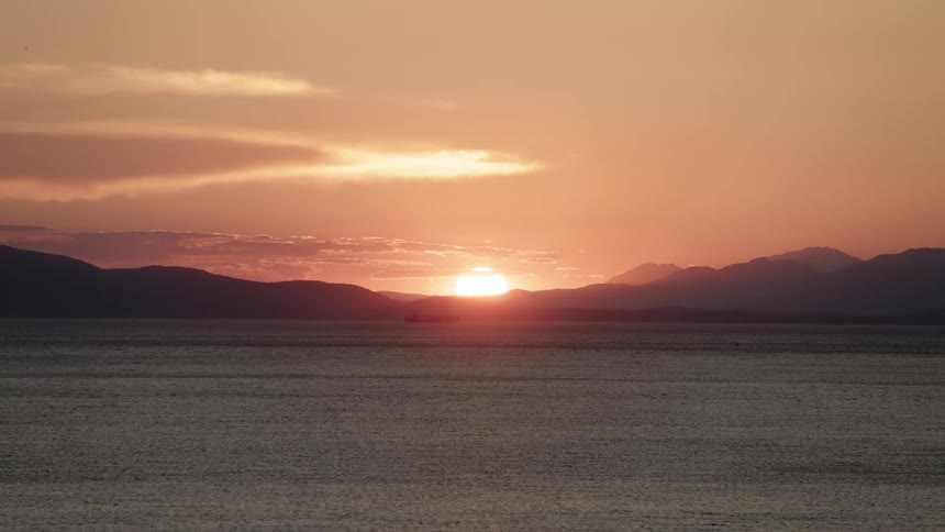 Setting sun shines from red sky sea with a ship sailing in the distance
