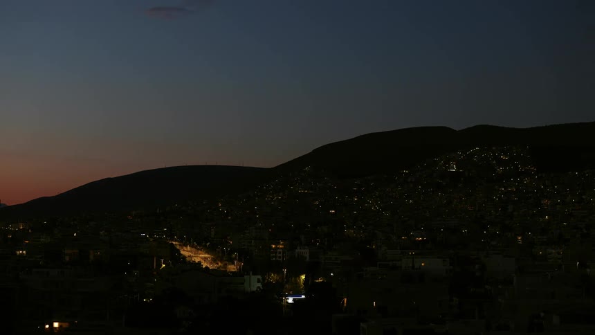 A timelapse of a  village on the slope of two hills with a main highway glowing with traffic into the night