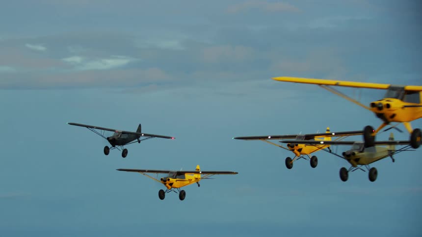 A group of small backcountry airplanes fly together in the sky as they head towards the backcountry