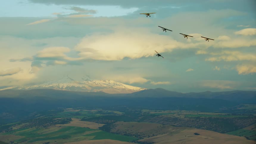 A group of small backcountry airplanes fly together with Mount Hood in the background