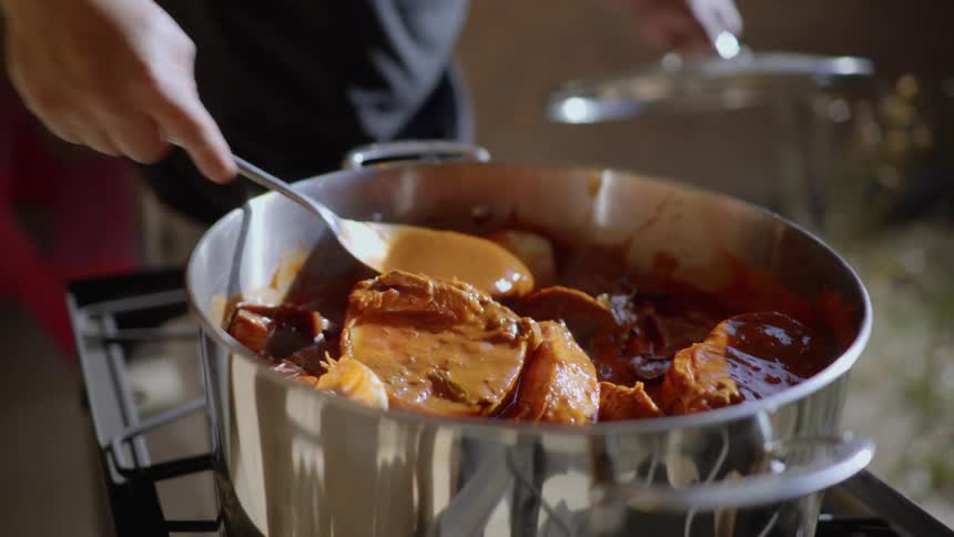 A man is stirring a pot of food that is cooking outside