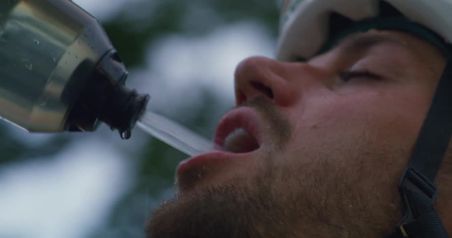 Cyclist wearing crash helmet drinks water from a portable water bottle