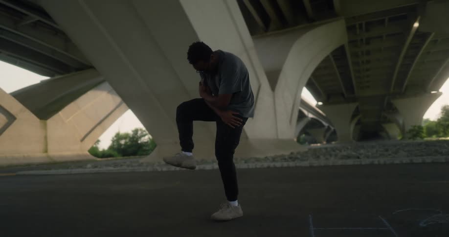 A man in sunglasses dances under a bridge during the day