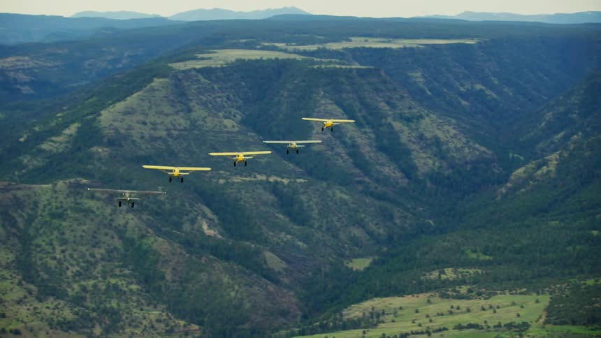Several small backcountry airplanes are flying in formation over the mountains
