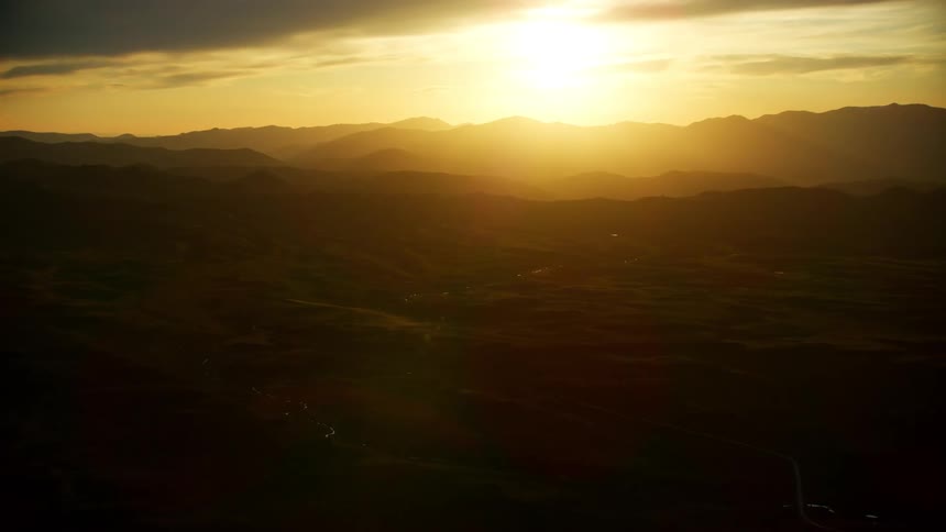Aerial view of sun going down and mountains silhouetted against the sun