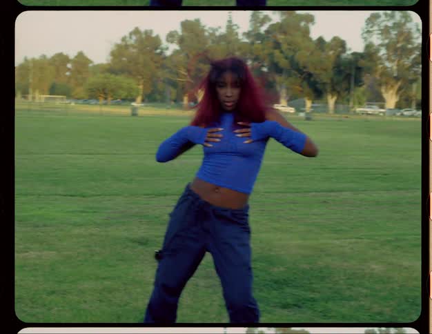 Woman with red hair blue top and sports pants dances on lawn in public park