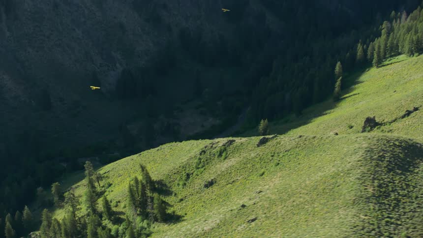 Small single engine cub crafter airplane fly over hills and forest in valley between mountains as seen from a helicopter above